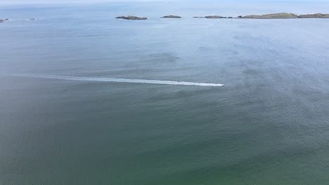 Una-Lancha-Rápida-Moviéndose-Rápidamente-A-Través-Del-Gran-Mar-Azul-En-Irlanda-Con-Una-Isla-Volcánica-En-El-Fondo---Antena