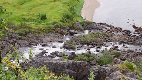 rocky river or stream flowing from the grasslands into the ocean on a beach in norway