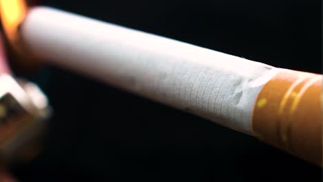 full fresh cigarette is lighten up by the lighter and left to be burned without smoking pov view extreme close up angled white and golden filter tailor made fag in pure darkness alone in nowhere