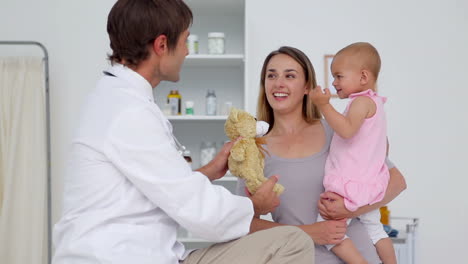 médico mostrando un oso de peluche a un bebé