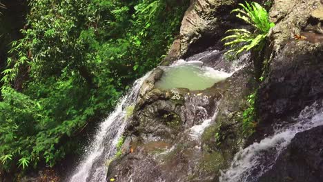 cascada gembleng fluye hacia abajo entre exuberantes rocas tropicales verdes