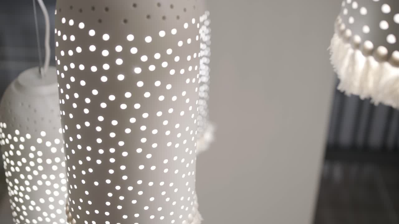 una serie de elegantes luces colgantes cilíndricas con una luz en cascada de patrón punteado a través de sus perforaciones, creando un ambiente lúdico y encantador en una escalera moderna