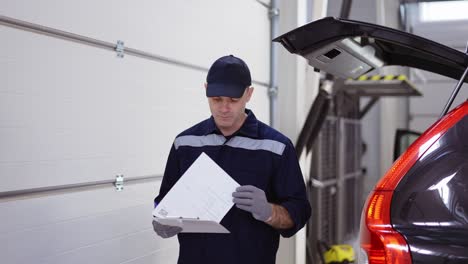 Man-in-uniform-in-a-auto-repair-shot-walking-around,-looking-to-his-notes