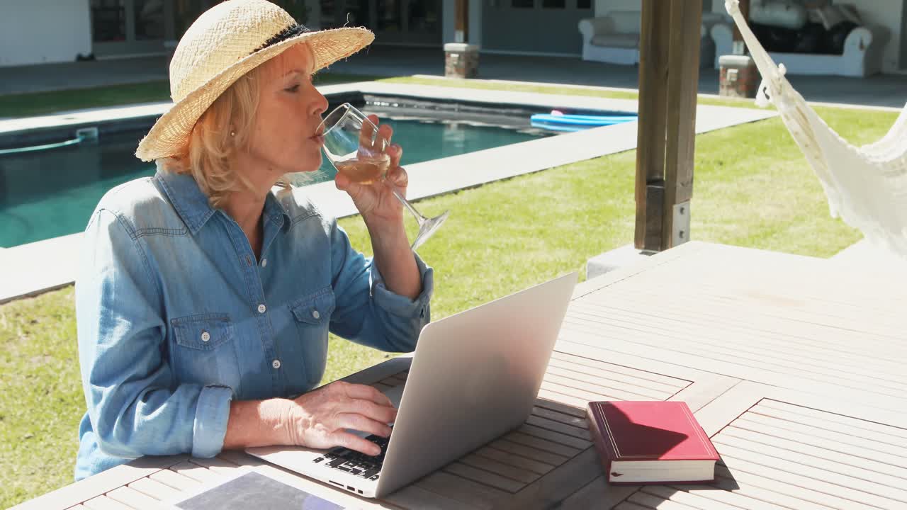 수영장 근처에 노인 여성이 노트북을 사용하고 있습니다.