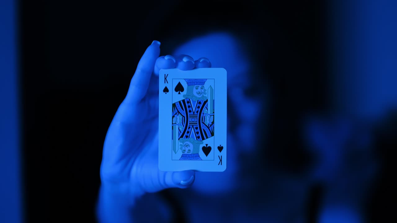 Focus on King of Spades card as woman slowly extends hand in blue neon light