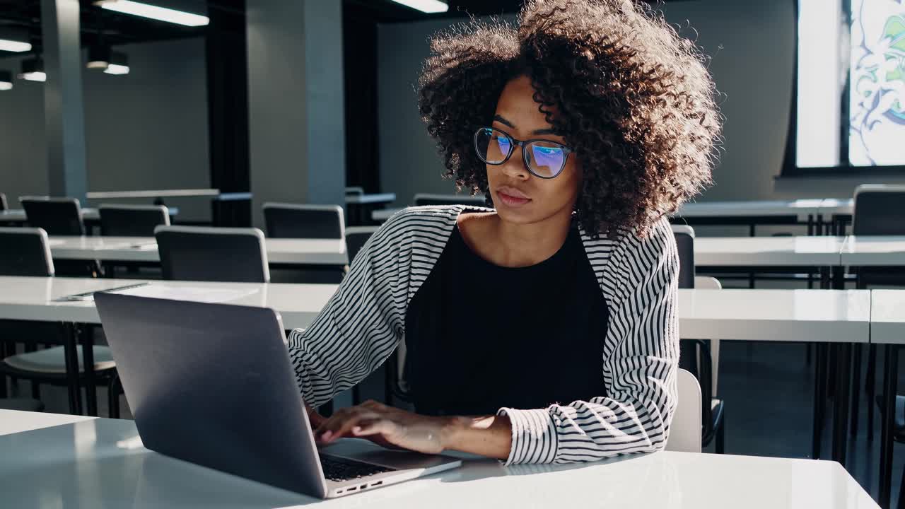 A focused woman works on a laptop in a modern office. The side angle captures her concentration