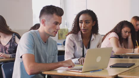 tutora femenina dando apoyo uno a uno al estudiante masculino que trabaja en el escritorio en la computadora portátil