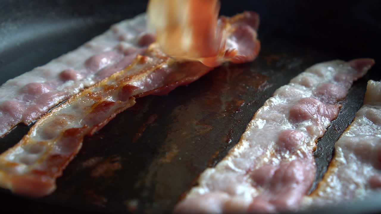 Man Chef cooking for breakfast: turning crispy bacon, rich in fat and colour, sizzling and smoking in a hot pan