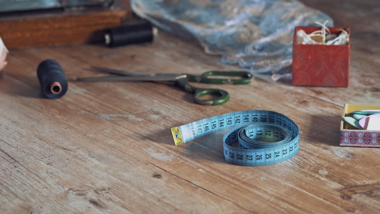 Seamstress is taking blue tape measure from the wooden table in atelier. Fingers of young female designer are taking the band with centimeter among sewing accessories.