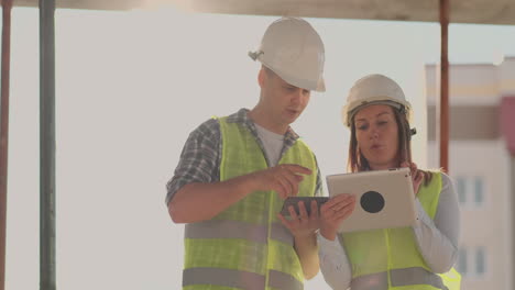 Building-in-construction-with-a-female-and-a-male-builders-constructors-engineers-walking-along-it