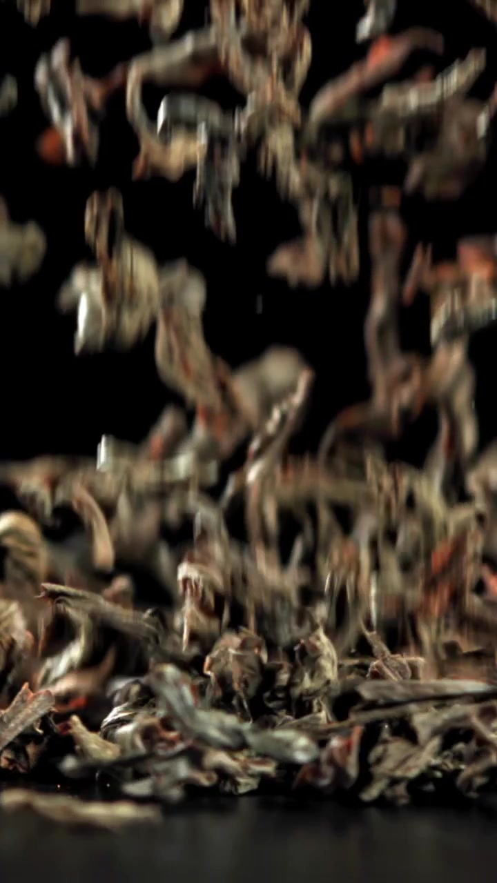 Dried tea leaves falling in slow motion on black background