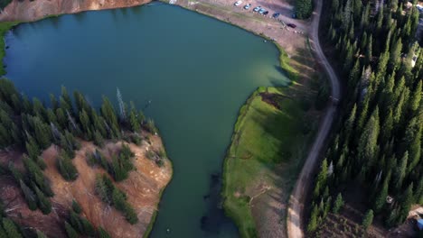 hermosa toma aérea de drones de un impresionante paisaje natural del lago anderson meadow embalse hasta beaver canyon en utah con un gran bosque de pinos, un camino de tierra y un estacionamiento para pescadores