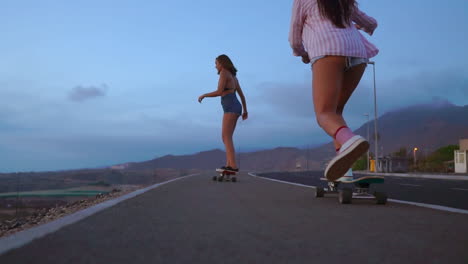 with mountains and a captivating sky in the backdrop, two friends engage in slow-motion skateboarding on a road at sunset. they're dressed in shorts