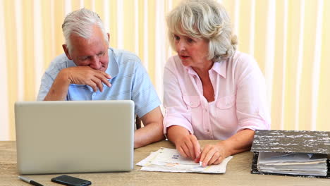 una pareja de ancianos pagando sus cuentas con una computadora portátil.