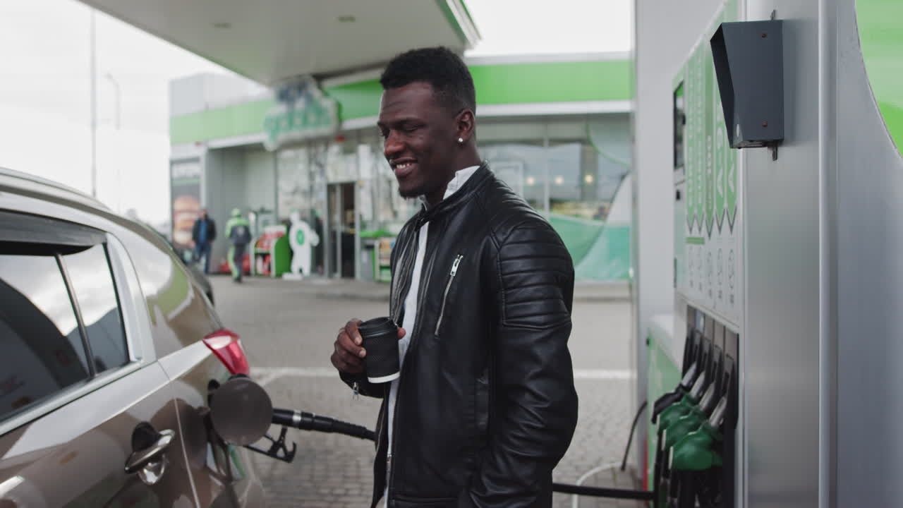 Ritratto di un ragazzo africano a una stazione di servizio con un caffè in mano mentre fa rifornimento all'auto durante un viaggio