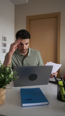 Man working at home office with laptop and paperwork