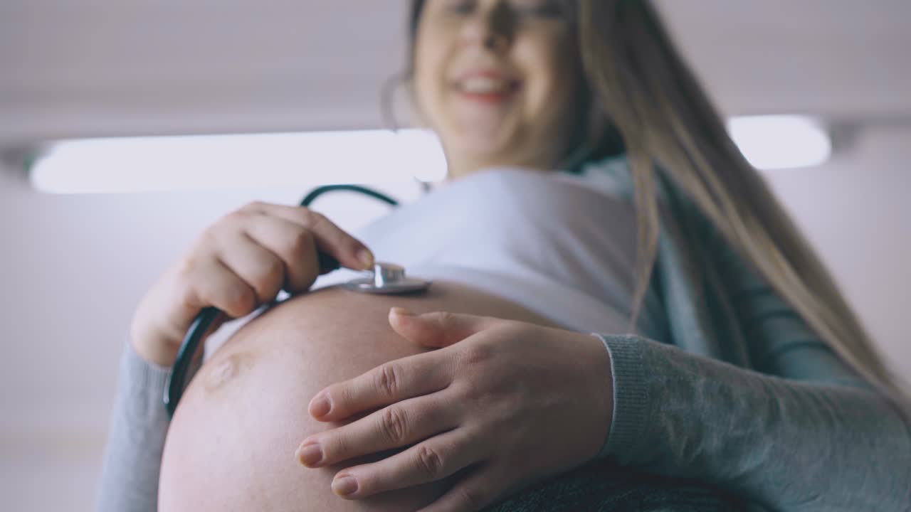 donna incinta usa lo stetoscopio per ascoltare il bambino in camera