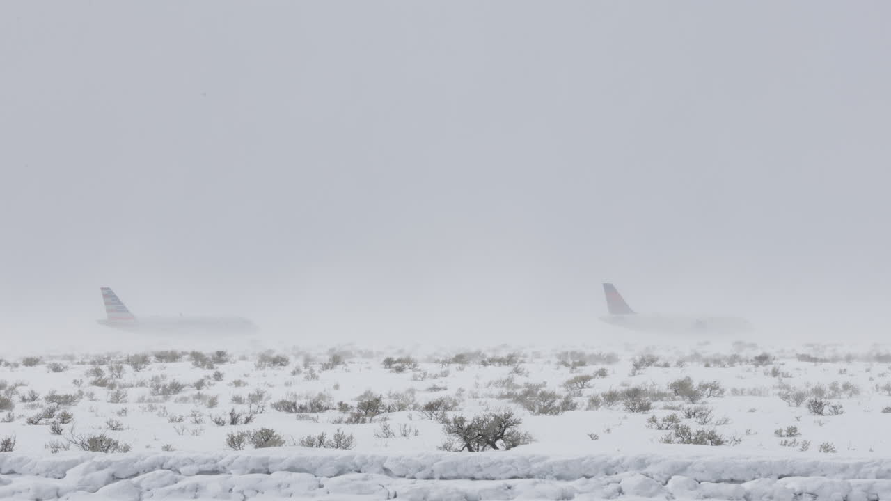 Telephoto shot of two airplanes waiting on the tarmac during an intense snow storm in western Wyoming. Shot in 4k 60fps