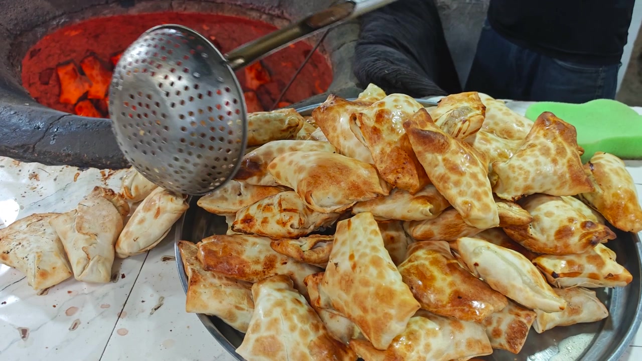 Fornaio che rimuove samsa appena sfornati da un tradizionale forno tandoor