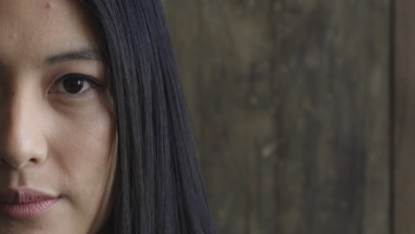 portrait close up of beautiful asian woman looking serious at camera on wooden background half face