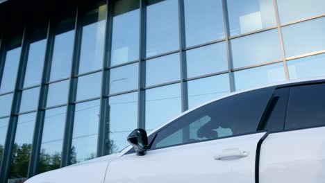 a businessman in a suit gets into the road in a white car near a glass building in the city