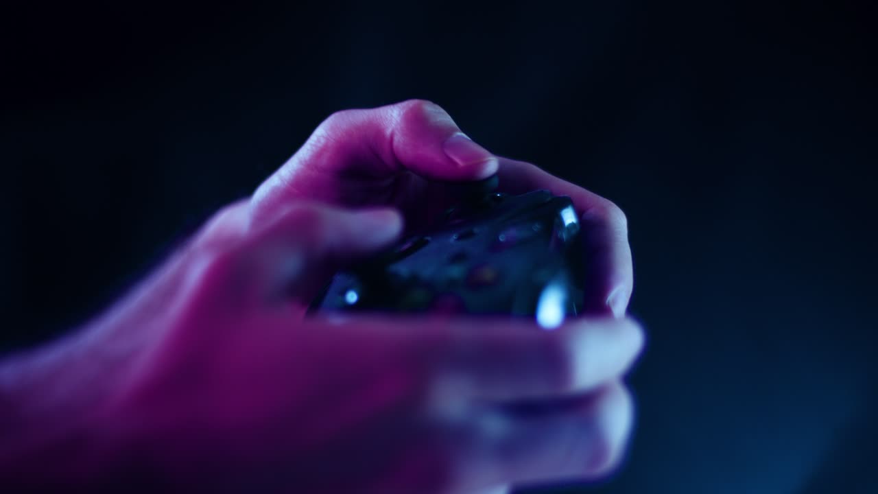 Playing video games in a darkened room with a black background close up on a controller buttons playing slowly blue lens flare