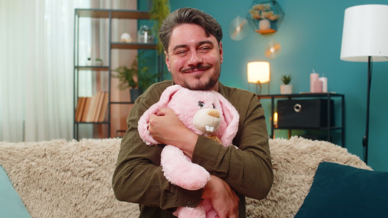 Middleaged man holding pink bunny toy smiling sadly missing child remembering past tender nostalgia