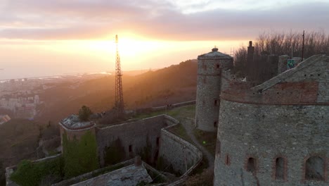 Forte-Sperone-at-sunset-with-Genoa-cityscape-in-the-background,-golden-light,-aerial-view