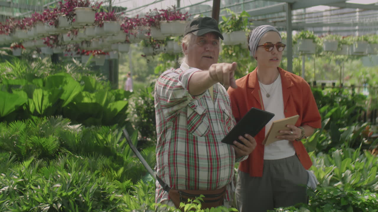 Nurseryman Using Tablet and Talking with Colleague in Greenhouse