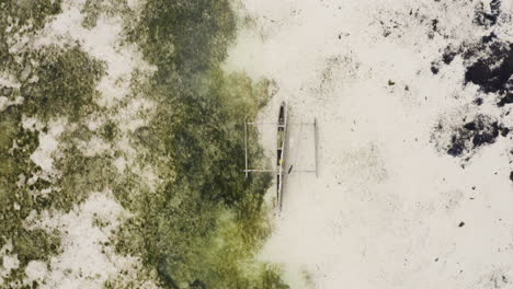 Wooden-catamaran-run-ashore-on-sandy-beach-with-seaweed-at-low-tide