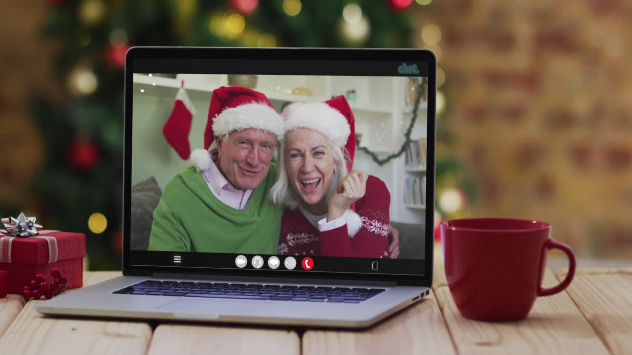 una pareja de alto nivel caucásica saludando en una videollamada en una computadora portátil, con un árbol de navidad