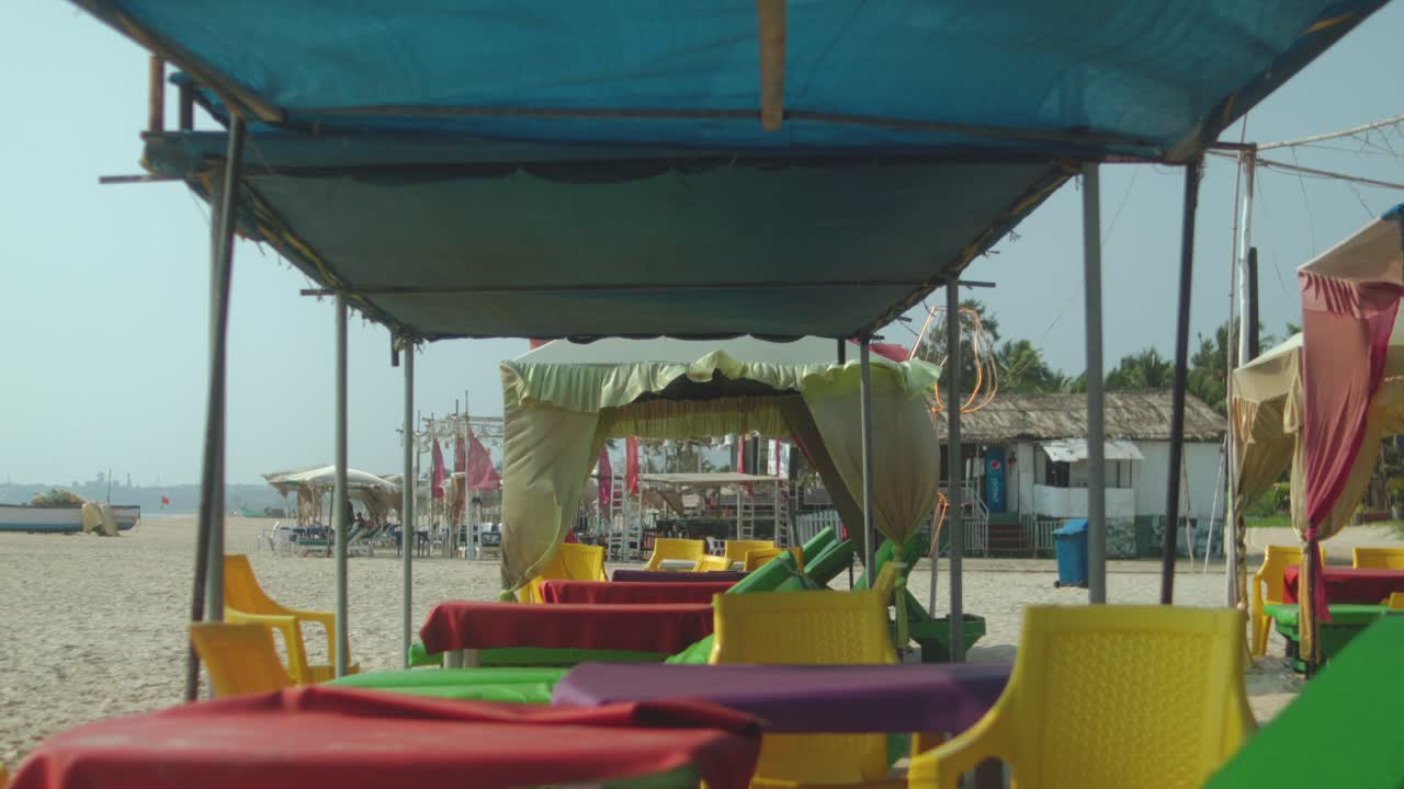 Vista fissa sotto tende da spiaggia con tavoli e sedie sulla sabbia.