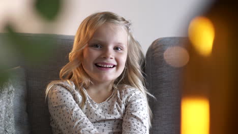 young caucasian girl smiles and laughs while sitting on couch in family home