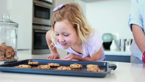 Mother-taking-hot-cookies-from-oven-with-little-girl-smelling-them