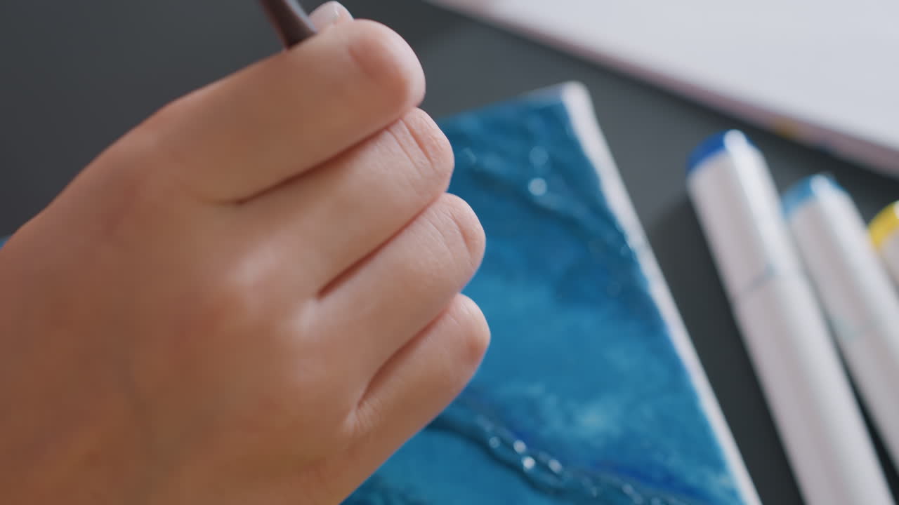 focused artist wielding brushes, precision painting with nearby implements, steady hand meticulously creating detailed line art, carefully controlled wrist movements with art tools and supplies ready
