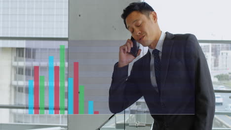 animation of multicolored bar graphs over asian man talking on cellphone in office