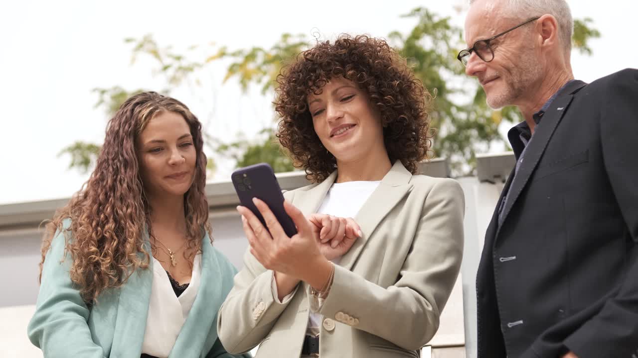 Happy businesswoman using cellphone while discussing with coworkers