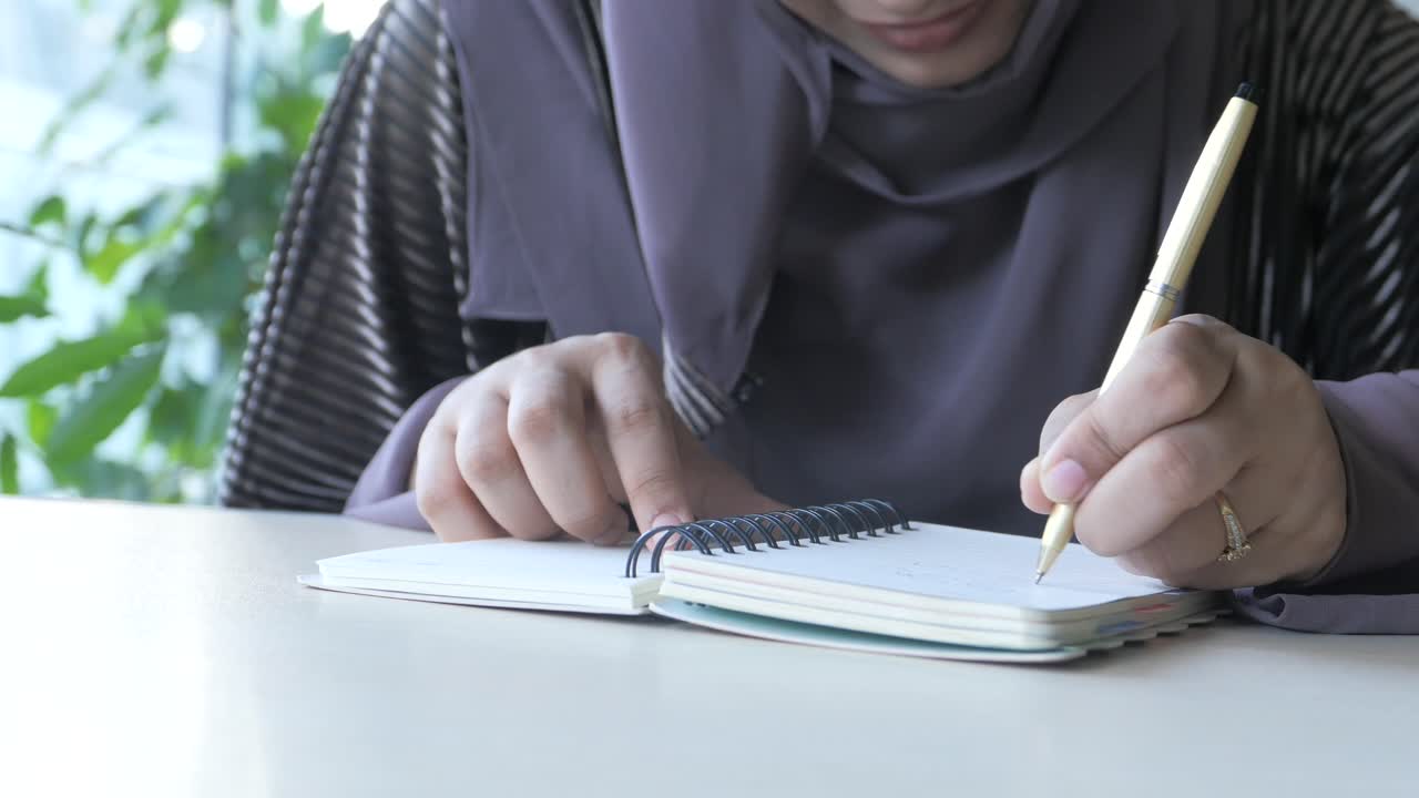 Wanita Berhijab Menulis di Buku Catatan