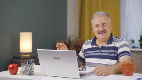 home office worker old man scratches his ears looking at camera.