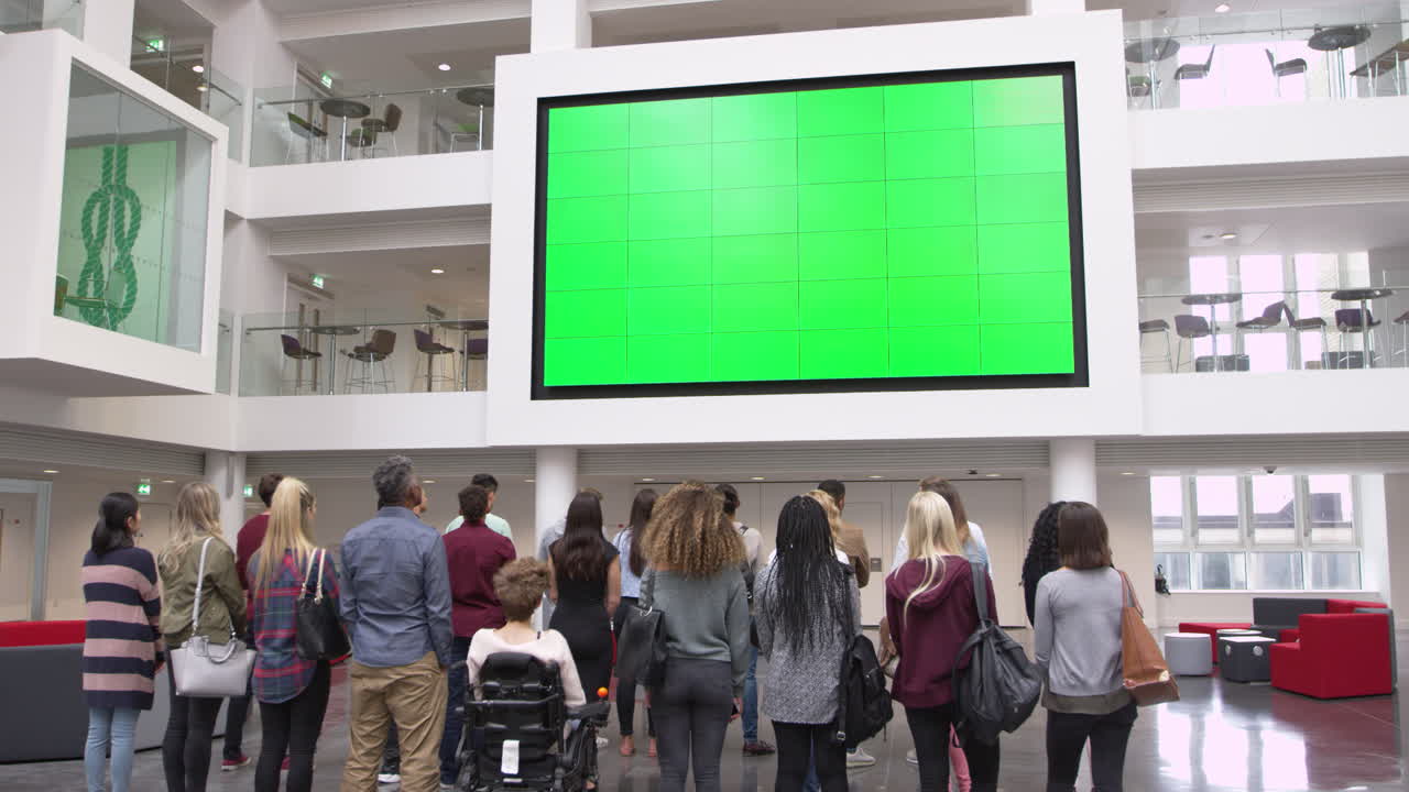 Students under big AV screen in university atrium, back view, shot on R3D
