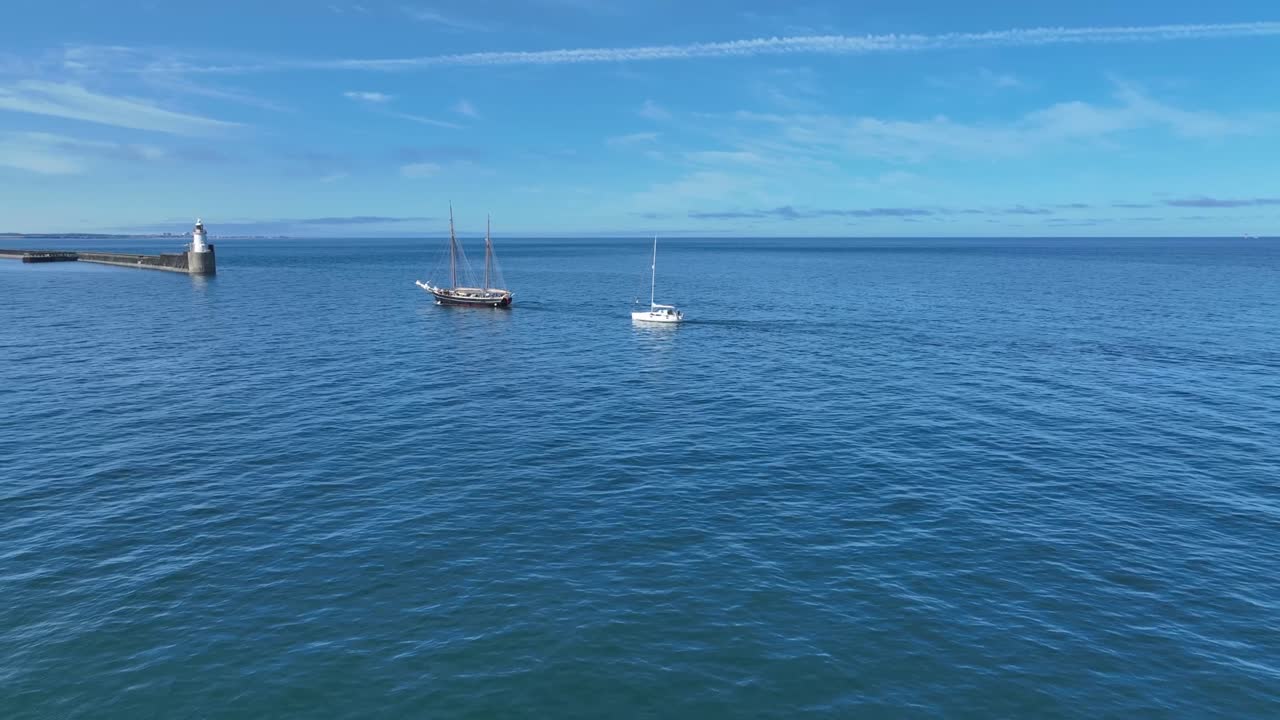 Drone clip of traditional tall ship and modern yacht sailing into harbour