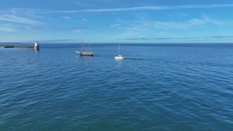 drone clip of traditional tall ship and modern yacht sailing into harbour