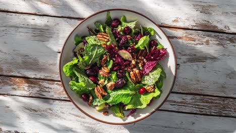 close up of a bowl of green salad with cranberries and pecans