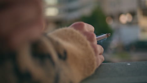 closeup hand holding cigarette at blurred urban backdrop. unrecognizable guy