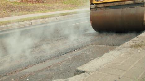 compactor wagon is driving over freshly poured and hot steaming asphalt to flatten it