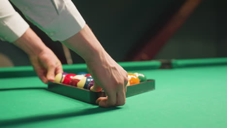 primer plano lateral de un hombre con camisa blanca posicionando cuidadosamente bolas de billar de colores bien dispuestas en formación de triángulo en la mesa de billar verde. sus manos rodan suavemente el rack