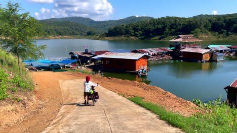 High-angle-shot-of-houseboats-on-lake-surrounded-by-hills-covered-with-green-vegetation-in-Nan-Province,-Thailand-on-a-sunny-day