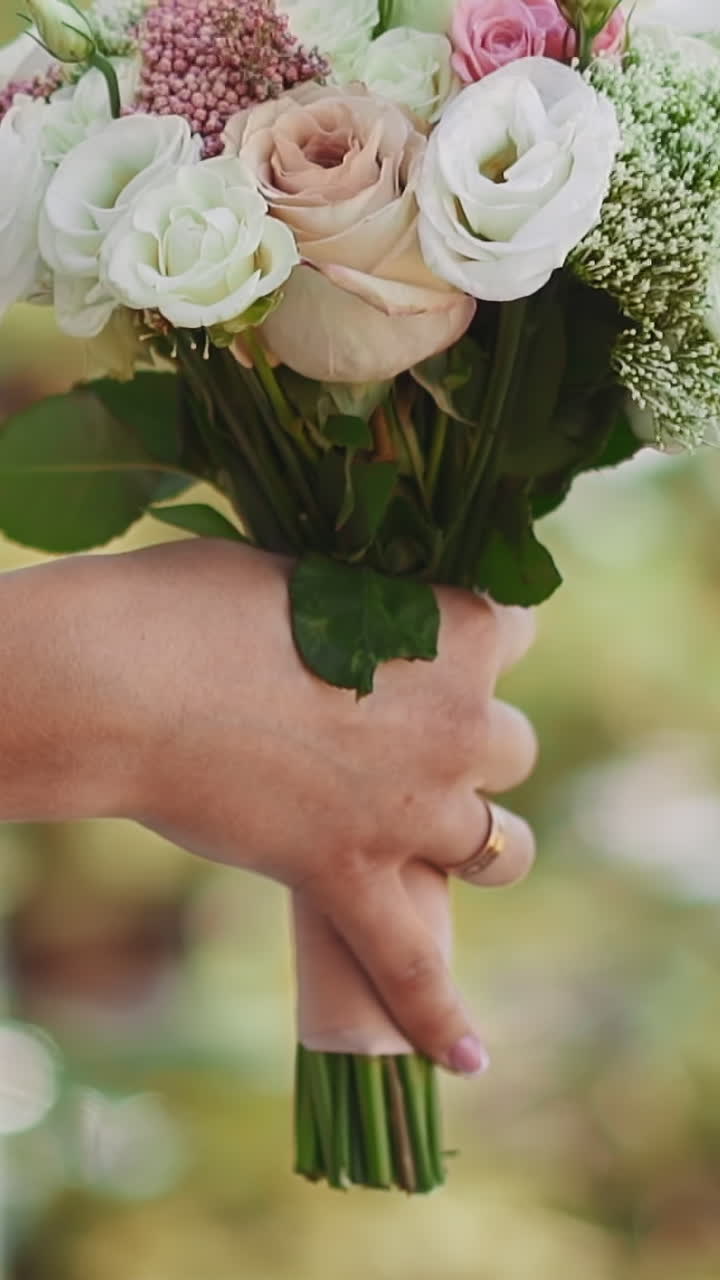 Bride with fresh roses bouquet leans on balcony metal railing in sunny summer park closeup slow motion. Wedding ceremony for young woman in green garden