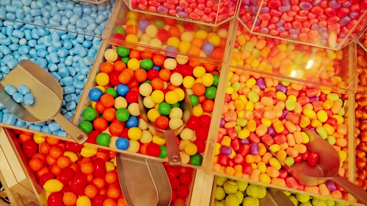 Slow sliding camera, vibrant candy assortment in shop bins with shiny scoops