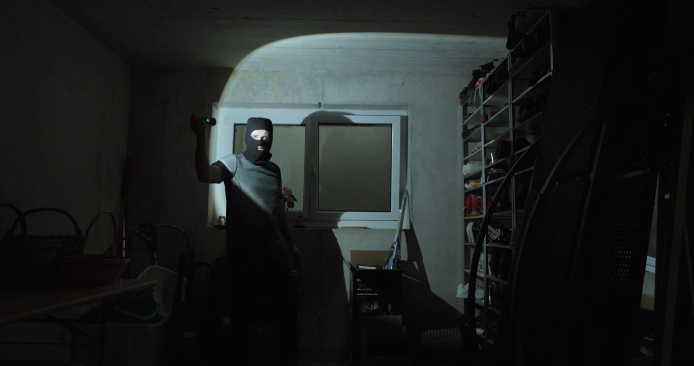 Scena interna notturna di un ladro all'interno di una stanza seminterrata che indica una finestra aperta usata per l'ingresso, che illustra un'intrusione domestica, un percorso di effrazione, un furto in abitazione